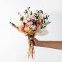 Preserved pink rose bouquet with cotton stems pampas grass and yellow flowers tied in rustic style on plain background.