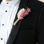 Elegant dried flower boutonniere with pink preserved flower rustic foliage and jute wrap styled on black background decor.