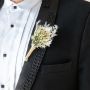 Closeup view of groom boutonniere with cream dried flowers and jute wrap pinned on black suit perfect for wedding decoration.