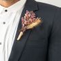 Boutonniere with pink dried flowers brown leaves and wheat grass wrapped in jute displayed on black background.