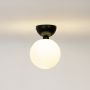 Black ceiling light with frosted glass globe shade glowing warmly on plain white background for home lighting.