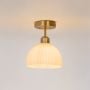 Ceiling light with brushed gold base and ribbed white glass dome shade glowing warmly on plain white background