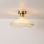 Ribbed glass and gold metal ceiling light illuminated on a clean white background showing warm bright glow.