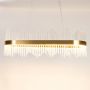 Gold metal chandelier with layered glass rods shown with lights on against a white background showing its glowing upscale design.