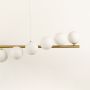 Closeup view of gold linear chandelier with staggered white globes in a front view against a white background with lights on perfect for modern designer lighting décor.
