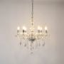 Crystal chandelier with lights on glowing warmly with glass detailing and crystal beads on white background.