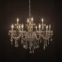 Crystal chandelier with candle lights and hanging crystal drops glowing warmly on black background view.