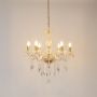 Gold chandelier with lights on glowing warmly with crystal detailing and glass body on white background.