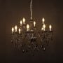 Elegant black chandelier with glossy arms and crystal droplets illuminated against black background decor.