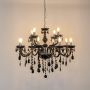 Black chandelier with crystal droplets glowing brightly on white background for elegant luxury home lighting.
