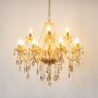 Golden chandelier with crystal detailing glowing on white background for luxury home decorative lighting.