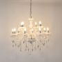 White chandelier with lights on glowing warmly with crystal hanging details and glass body on white background.