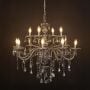 Black chandelier with lights on glowing warmly with crystal drops and glass arms against a black background.