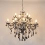 Black chandelier with lights on glowing warmly with detailed glass arms and crystal beads on white background.