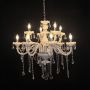 White chandelier with lights on glowing warmly with crystal drops and glass body against a black background.