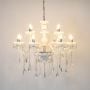 White chandelier with lights on glowing warmly with hanging crystal details and glass arms on white background.