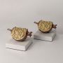 Set of golden pomegranate sculptures on marble bases turned on styled together for elegant interiors.