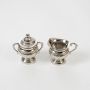 Silver sugar bowl and creamer set with decorative handles and pedestal bases displayed on a white background.

