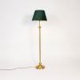 Golden stand floor lamp with green fabric shade glowing softly against plain white background.