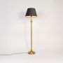 Golden stand floor lamp with black fabric shade glowing warmly against plain white background.