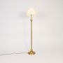 Classic golden stand floor lamp with pleated white shade glowing warmly on white background.