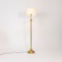 Elegant golden stand lamp with pleated white shade glowing softly against plain white background.