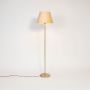 Stylish floor lamp with beige fabric shade and golden stand glowing warmly against white background.