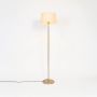 Floor lamp with pleated white shade and golden stand glowing warmly against white background.