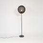 Contemporary black floor lamp with round woven rattan globe shade glowing warmly on white background.