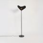 Contemporary black floor lamp with unique rattan woven shade glowing warmly on plain white background.