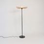 Contemporary black floor lamp with handcrafted rattan leaf shade glowing warmly on white background.
