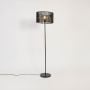 Contemporary black floor lamp with round woven rattan shade glowing warmly on plain white background.
