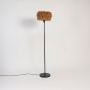 Wicker floor lamp with handwoven rattan shade on sleek black stand against white background.