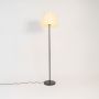 Modern floor lamp with pleated cream fabric shade and slim black stand glowing against white background.