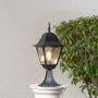Classic black pillar lamp glowing on stone pillar creating warm illumination for outdoor home entrance and pathway lighting.