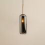 Smoked grey glass cylindrical pendant with warm glowing inner diffuser and gold fitting shown on a white background for modern decor styling.