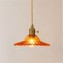 Amber ruffle glass pendant lamp illuminated warmly on a white background showcasing its vibrant glow and brass fitting.