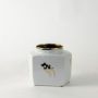 Small white ceramic jar with gold lid and minimal gold abstract design on simple white background for décor.