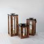 Set of rustic wooden lanterns in small medium and tall sizes with candles lit for indoor outdoor decor.