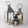 Set of tall medium and small silver lanterns with candles lit perfect for modern indoor outdoor decor.