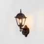 Illuminated black metal outdoor wall light on dark background highlighting classic lantern design and warm welcoming glow.