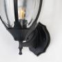Closeup of black outdoor wall sconce with curved glass panels showing traditional coach lantern design and craftsmanship.