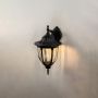 Illuminated black outdoor wall sconce on white background showcasing downward lantern with clear glass vintage style fixture.