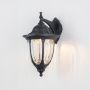 Black downward outdoor wall lantern glowing on black background highlighting traditional coach style exterior lighting warm glow.