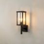Outdoor wall light with black metal frame and clear glass shade switched on against plain white background.