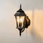 Black wall lantern light with clear glass panels shown glowing against a plain white background.