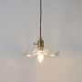 Clear wavy glass pendant light with brass holder glowing warmly on white background for decorative home lighting.