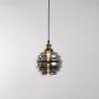Smoked glass pendant light with warm glow hanging against a clean white background highlighting its rippled round shade and brass holder with a soft illuminated effect.