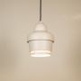 White industrial pendant light with ribbed detailing hanging against plain background with light on for clean minimal décor.
