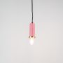 Pink pendant light turned on with glowing bulb and brass accent displayed on clean white background.